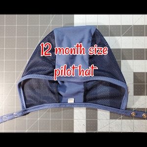 May include: A blue and black 12 month size pilot hat with a mesh panel and adjustable straps. The hat has a label that says "12mo".
