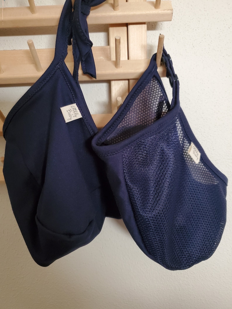 May include: Two dark navy blue fabric pouches with tie closures and snap buttons. One pouch is made of solid fabric, while the other features a mesh panel. Both items have a small white rectangular tag with the text Jelly Baby printed in black.