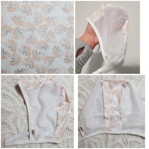 May include: White baby bonnet with a mesh front and a rainbow pattern in pastel colors. The bonnet has a tie closure and a small tag. The rainbow pattern is repeated on the bonnet's lining.