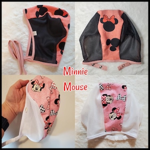 May include: Pink and black fabric baby bonnet with a Minnie Mouse print. The bonnet has a mesh lining and ties at the back.