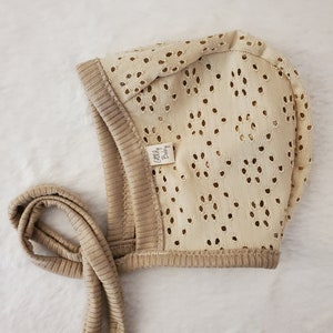 May include: A beige crocheted baby bonnet with a tie. The bonnet has a small label that says "Cozy Baby".