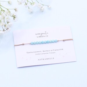 Peut inclure: Un bracelet de perles en amazonite bleu clair sur un cordon en polyester beige, présenté sur une carte blanche avec le texte amazonite SINCÉRITÉ, Épanouissement, Bonheur et Tranquillité, Cordon polyester français et A T R A M E L L E.
