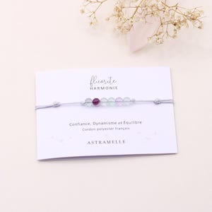Peut inclure: Un bracelet de perles de fluorite colorées, avec des perles violettes, vertes et transparentes. Le bracelet est présenté sur une carte blanche avec le texte "fluorite HARMONIE" et "Confiance, Dynamisme et Équilibre".