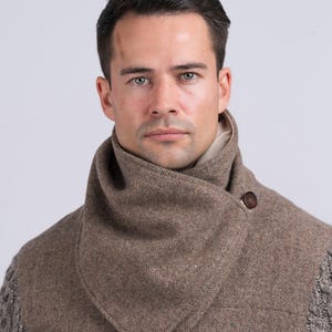 May include: A brown herringbone patterned scarf with a button closure. The scarf is folded into a triangle shape and worn around the neck.