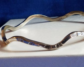 May include: A silver wavy bangle bracelet with a leaf pattern etched into the metal. The bracelet is marked "925" on the inside.
