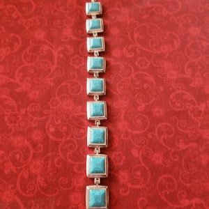 May include: A silver bracelet with turquoise stones. The bracelet has a square shape and is made of metal.