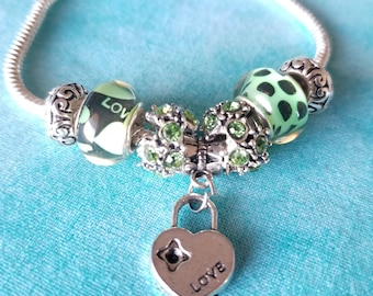 May include: A silver charm bracelet with a heart-shaped lock charm that says "LOVE". The bracelet has green and white patterned beads and green crystal beads.