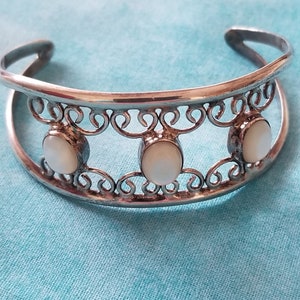 May include: A silver bracelet with a delicate, ornate design featuring three white mother-of-pearl stones.