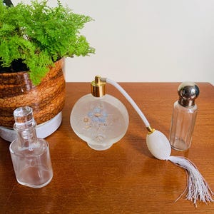 May include: Three vintage glass perfume bottles. The bottle in the centre is frosted glass with a floral design and a gold top. The bottle on the left is clear glass with a simple design. The bottle on the right is clear glass with a silver top.