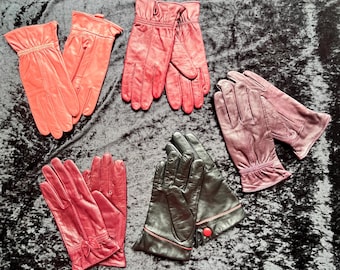 Puede incluir: Una colección de cinco pares de guantes de cuero en varios colores, incluyendo naranja brillante, rojo, rojo oscuro y negro. Los guantes presentan detalles de costura, puños fruncidos y un par incluye un pequeño lazo decorativo.