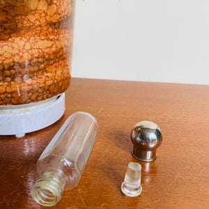 May include: A clear glass bottle with a silver top and a separate glass stopper. The bottle is lying on a wooden surface.