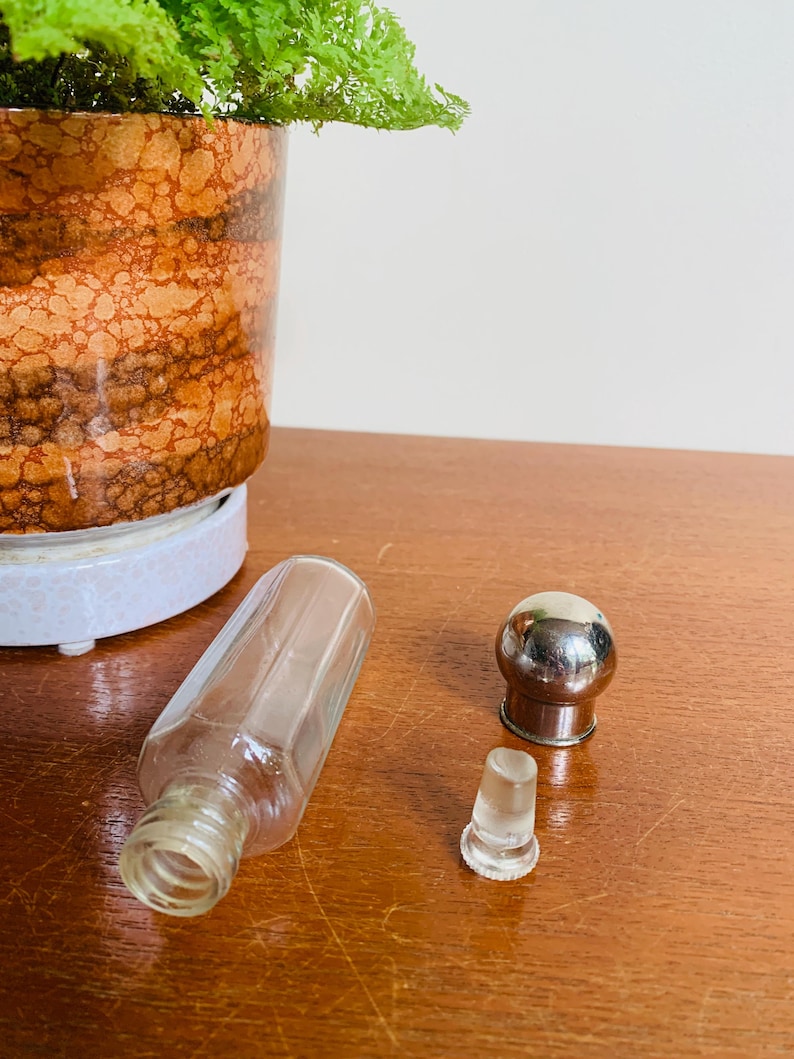May include: A clear glass bottle with a silver top and a separate glass stopper. The bottle is lying on a wooden surface.