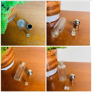 May include: Four glass bottles with stoppers. The bottles are clear and have a cylindrical shape. The stoppers are silver and have a round shape. The bottles are on a wooden surface.