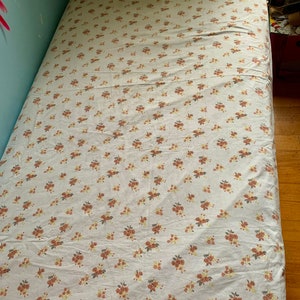 May include: A white twin-sized bed sheet with a small floral pattern in shades of brown, pink, and green.