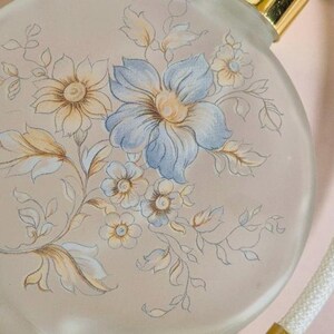 May include: A vintage glass perfume bottle with a floral design. The bottle is round and has a gold cap. The floral design is in shades of blue, yellow, and white.