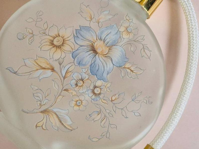 May include: A vintage glass perfume bottle with a floral design. The bottle is round and has a gold cap. The floral design is in shades of blue, yellow, and white.