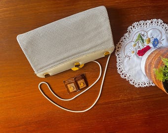 Puede incluir: Un bolso de mano de malla blanca con ribete de cuero blanco liso y herrajes de metal dorado. El bolso cuenta con una correa de hombro blanca fina y dos pequeñas etiquetas cuadradas con la letra G impresa en oro sobre fondo marrón.