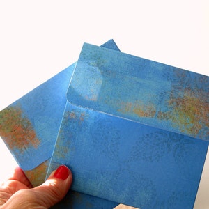 May include: Two blue envelopes with a textured, faded floral pattern. The envelopes are folded and stacked on top of each other.
