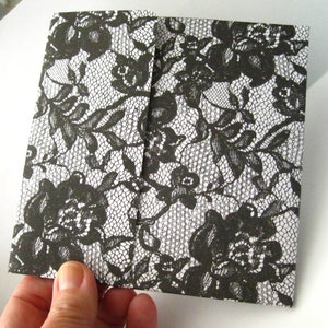 May include: Black and white lace pattern on a folded card. The lace pattern is a floral design.