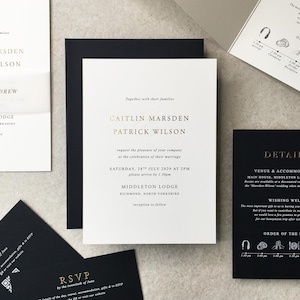 May include: Elegant wedding stationery set featuring a white invitation with gold text, a black RSVP card, and a details card. The invitation includes names, date, and location. The set is arranged on a neutral surface.