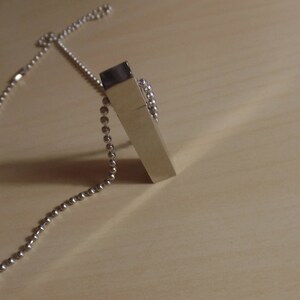 Puede incluir: Un collar de cadena de plata con un colgante rectangular de plata.