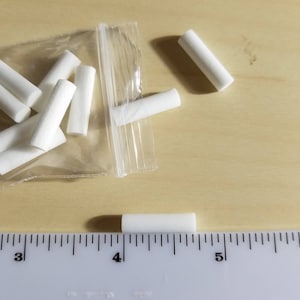 May include: A close-up of a bag of white cigarette filters, with a ruler showing the size of the filters. The filters are about 1 inch long.