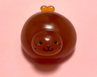 Könnte beinhalten: Ein braunes, weiches Spielzeug in Form einer Robbe mit einem kleinen orangefarbenen Herzen oben drauf. Die Robbe hat ein süßes Comic-Gesicht mit schwarzen Augen und einem Lächeln.