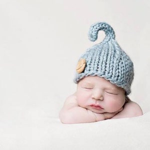 May include: A sleeping newborn baby wearing a light blue knitted hat with a wooden button and a curled brim.