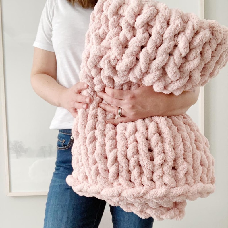 May include: A soft, pink, chunky knit throw blanket. The blanket is made with a thick yarn and has a fluffy texture.