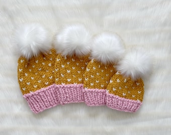 May include: Four knitted hats with white pom poms. The hats are yellow with white polka dots and pink brims.