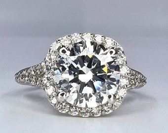 May include: A silver engagement ring with a large, round, clear diamond center stone surrounded by a halo of smaller diamonds. The band is also set with smaller diamonds.