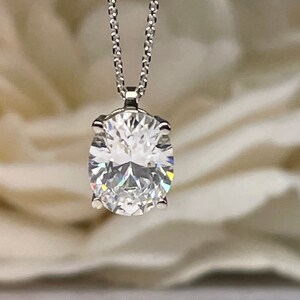 May include: A silver necklace with a large, oval-cut diamond pendant. The diamond is set in a four-prong setting and sparkles brightly. The chain is delicate and hangs from the pendant.