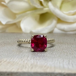 May include: A gold ring with a red square-shaped gemstone. The ring has a twisted band.
