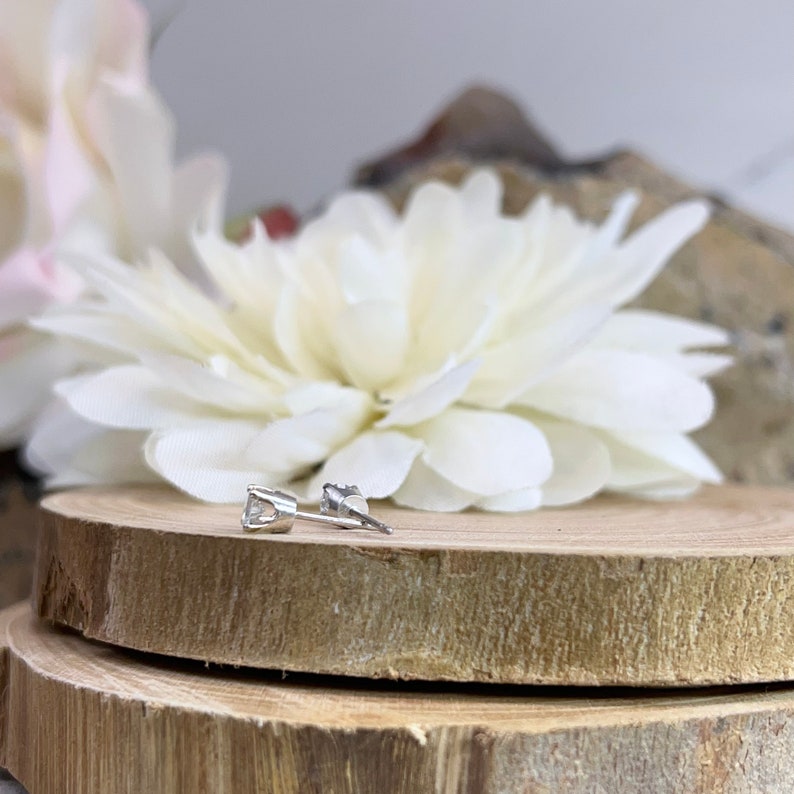 May include: A pair of silver stud earrings with a clear round gemstone in the center.