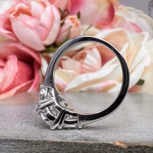 May include: A silver ring with three large diamonds set in a prong setting. The ring is on a gray surface.