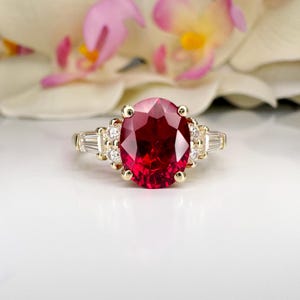 May include: A gold ring with a large oval ruby gemstone surrounded by smaller diamonds. The ring is set in a prong setting.