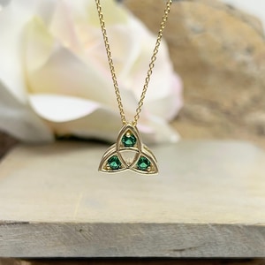 May include: A gold Celtic knot pendant necklace with three green gemstones. The pendant is in the shape of a trinity knot.