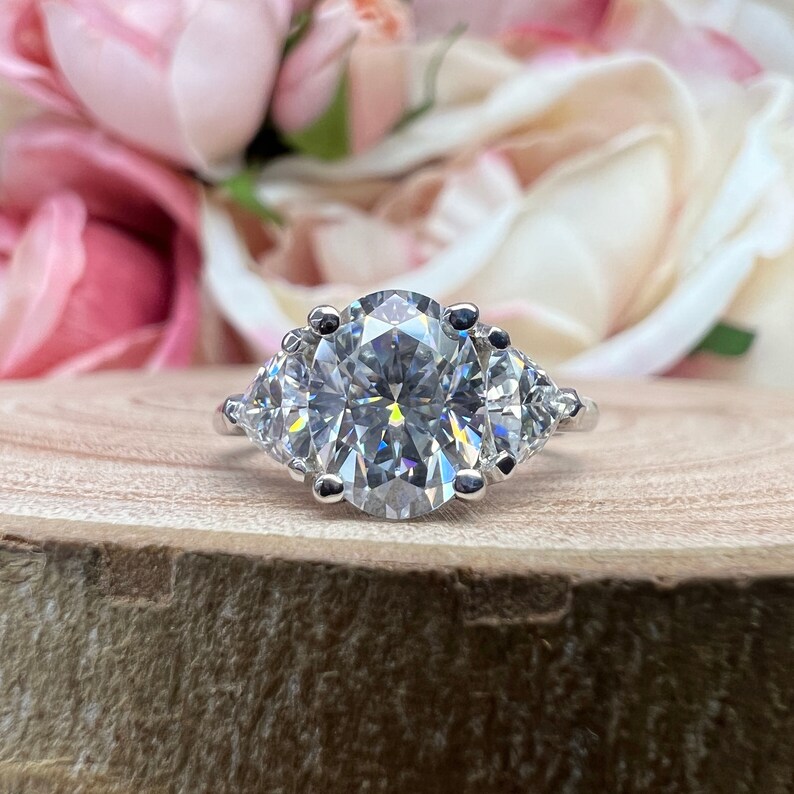 May include: A silver ring with a large oval-shaped diamond in the center and two smaller triangular diamonds on either side.