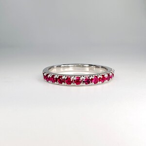 May include: A white gold band ring with a row of red ruby gemstones.