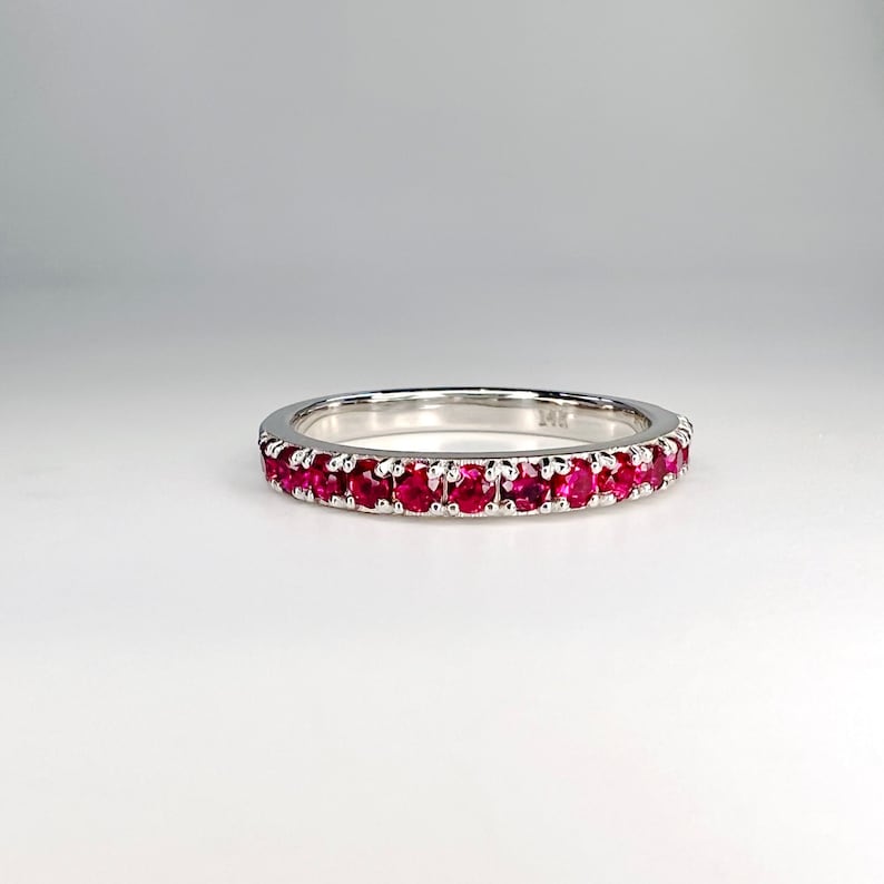 May include: A white gold band ring with a row of red ruby gemstones.