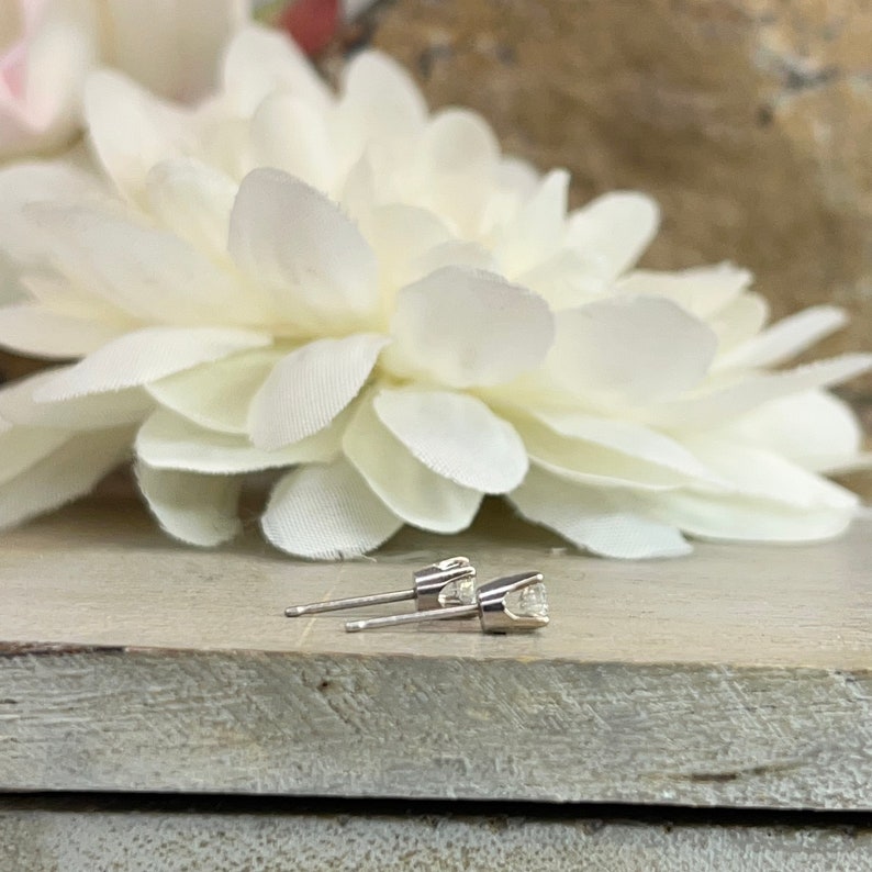 May include: A pair of silver stud earrings with a small, clear gemstone in the center of each earring.