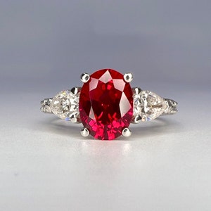 May include: A silver ring with a large oval-shaped ruby gemstone surrounded by two smaller pear-shaped diamonds.