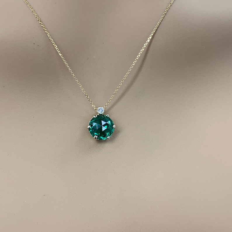 May include: A gold chain necklace with a green gemstone pendant. The pendant is surrounded by smaller diamonds.