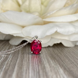 May include: A silver chain necklace with a large oval-shaped ruby pendant.