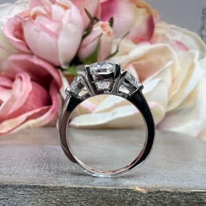 May include: A silver ring with a large, round, clear center stone and two smaller, triangular, clear stones on either side.