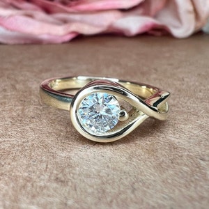 May include: A gold ring with a large, round, clear gemstone set in a unique, infinity-shaped design.