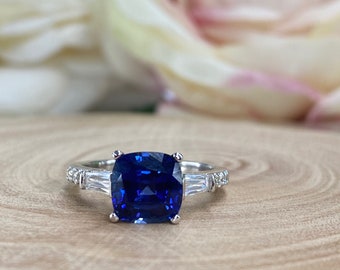 Op de afbeelding: Een zilveren ring met een grote, diepblauwe kussenvormige saffier, omringd door kleinere baguette-diamanten.