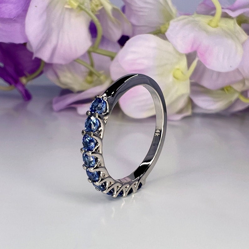 May include: A silver band ring with a row of blue sapphires set in a delicate, intricate design. The ring is marked with "14K" on the inside.
