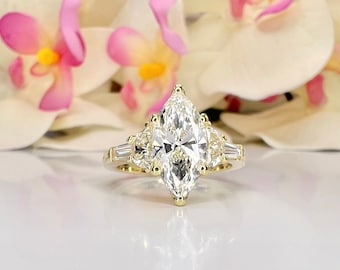 Könnte beinhalten: Ein goldener Verlobungsring mit einem großen, markisenförmigen Diamanten als Mittelstück und zwei kleineren birnenförmigen Diamanten auf jeder Seite.