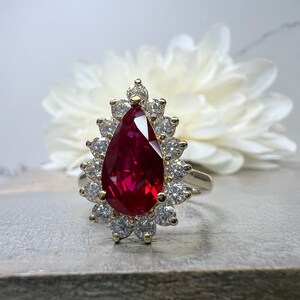 May include: A pear-shaped ruby ring with a halo of smaller diamonds set in gold.
